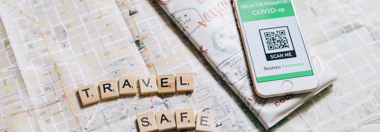 A phone disaplying a health passport app and QR code beside Scrabble letters spelling the words 'Travel Safe'