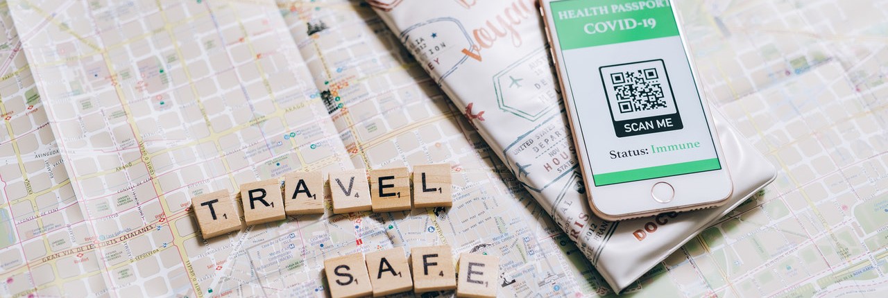 A phone disaplying a health passport app and QR code beside Scrabble letters spelling the words 'Travel Safe'