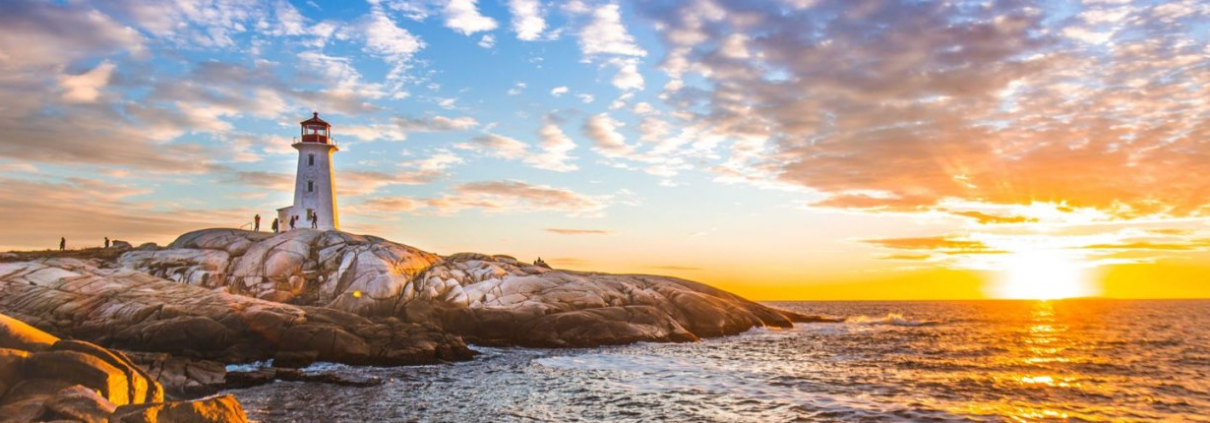 A lighthouse stands by a rocky coastline in front of a sunrise