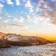 A lighthouse stands by a rocky coastline in front of a sunrise