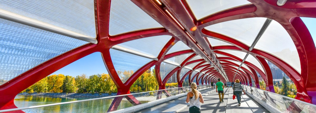 People job and walk across a bridge with a curving, red steel canopy overhead