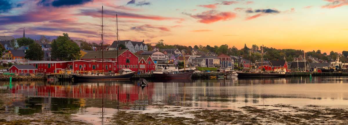 A historic waterfront at sunrise, with several boats moored at the shore