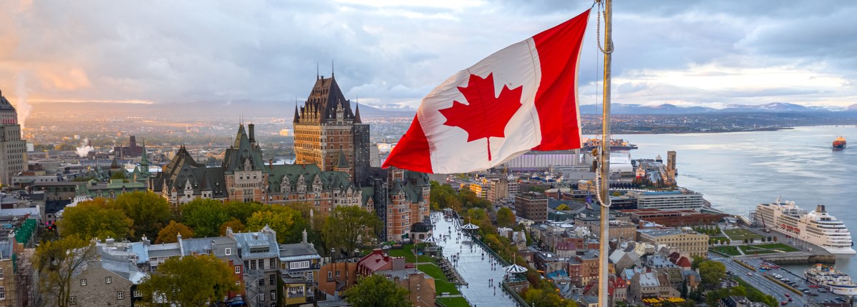 A Canadian flag flies in front of a backdrop of the historic centre and waterfront of a Canadian city