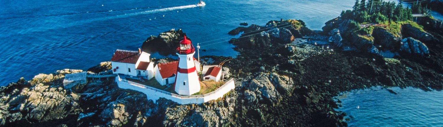 A red-banded white lighthouse sits atop a rocky outcrop in New Brunswick, Canada