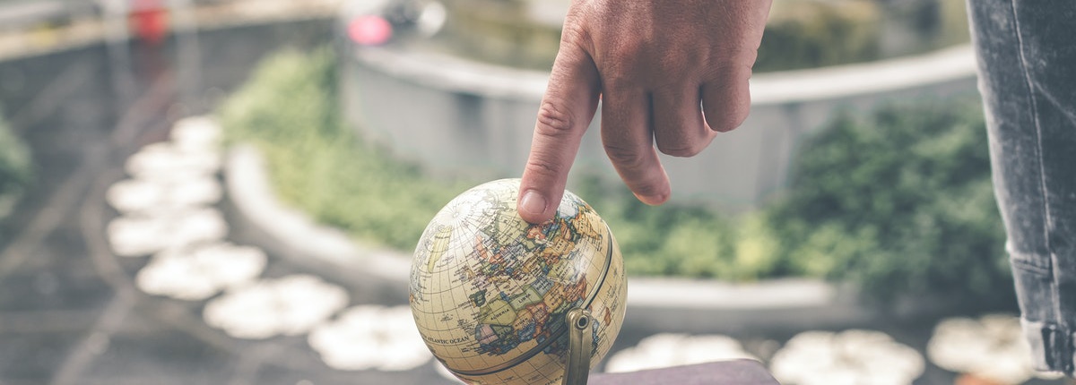 A man's hand places an index finger on a small globe