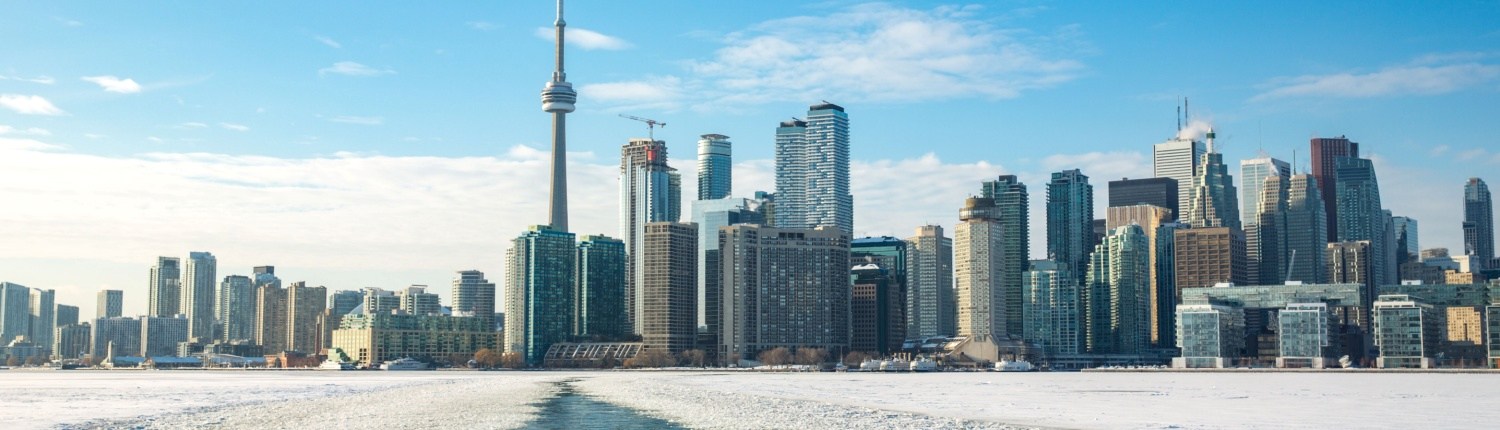 A boat's wake cuts through thin ice on the top of a lake, with the Toronto skyline in the background